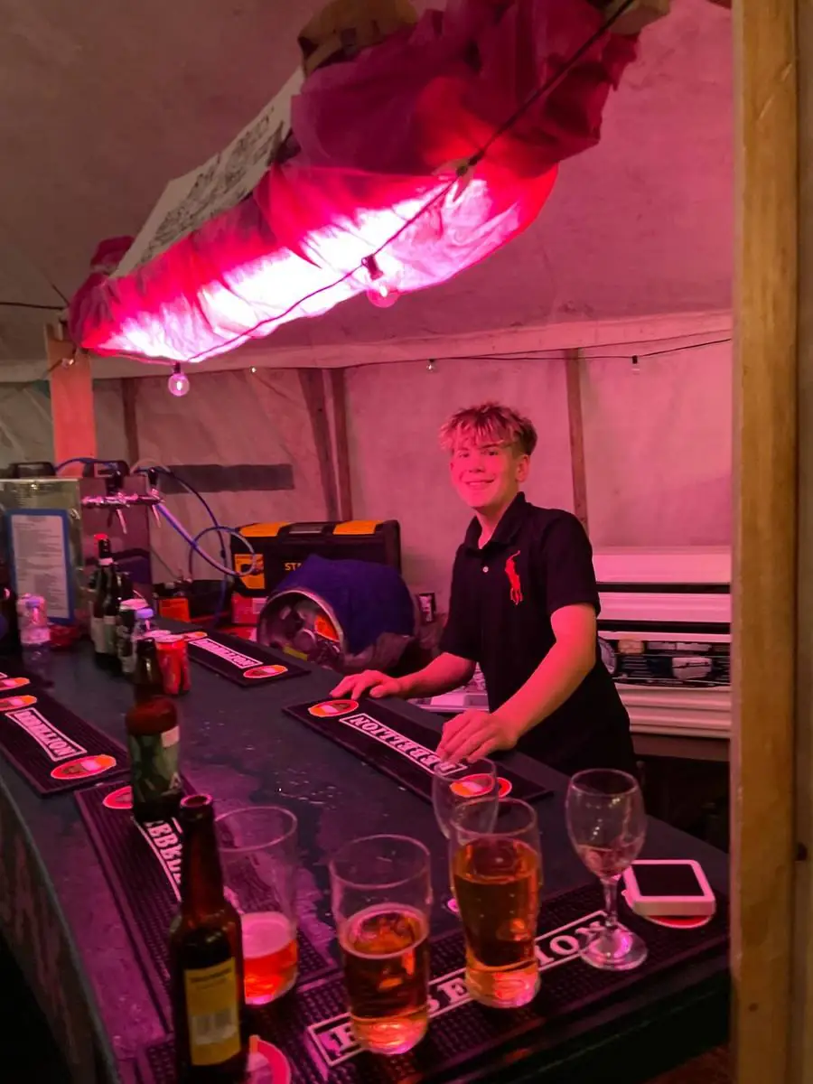 Behind the bar at the summer social: a club member serving drinks under pink festival lighting