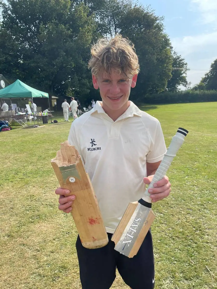 A junior player grinning and holding up a cricket bat snapped clean in two