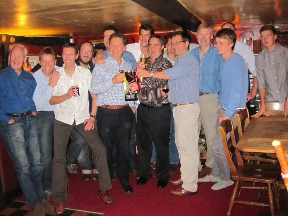 Swyncombe players and members raising the cup together in the pub, ribbons in club maroon and gold