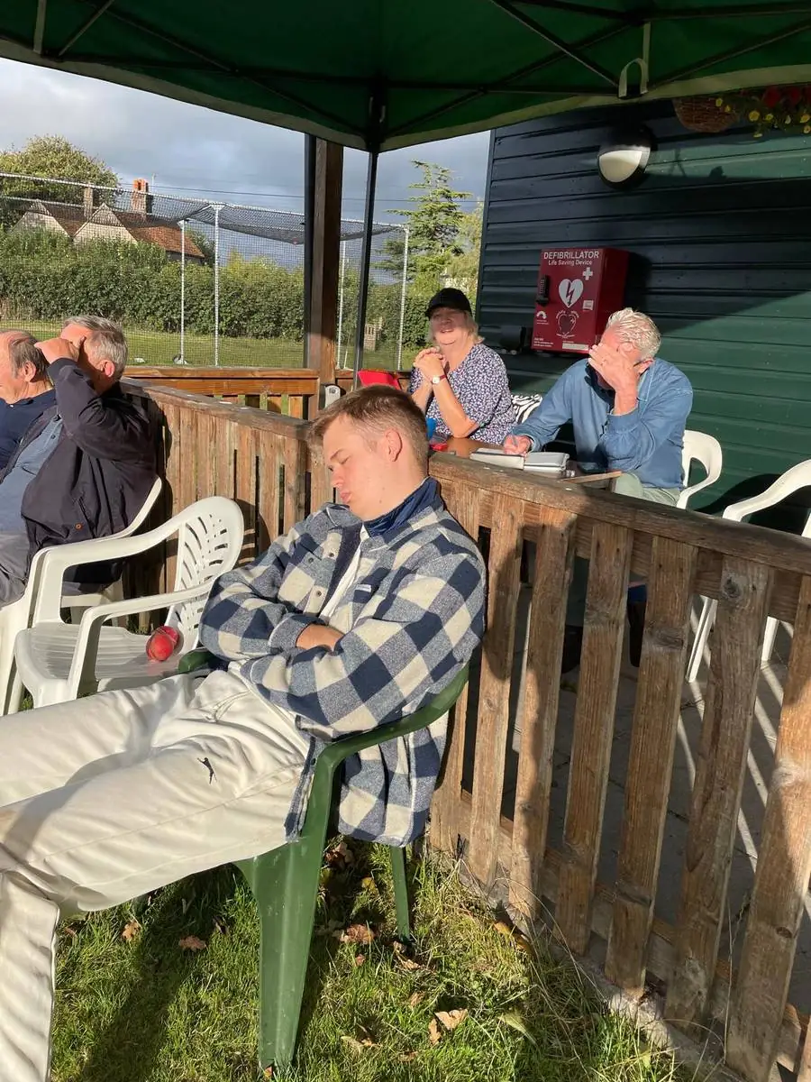 A player fast asleep in a chair on the pavilion terrace while spectators chat behind