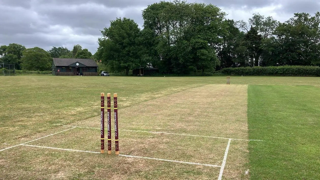 The pitch at the Field of Dreams, with Swyncombe CC's maroon-wrapped stumps in the foreground and the green pavilion beyond