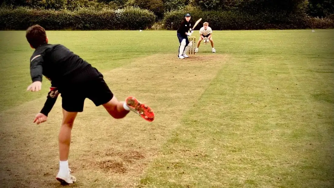 Training on the square: a bowler in mid follow-through with batter and keeper waiting at the far end